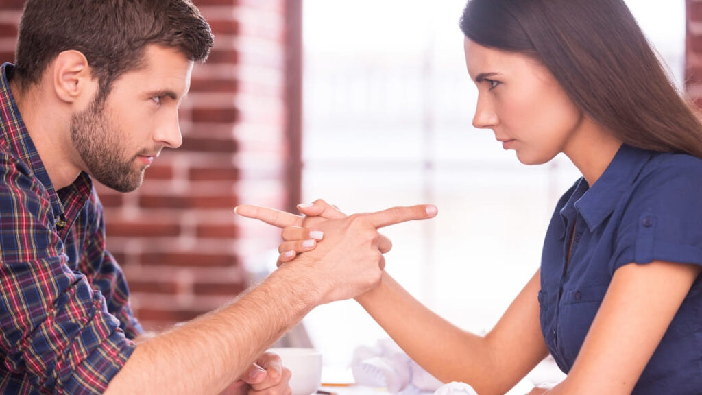 向かい合って手を握り合い、互いに人差し指を向け合って険しい表情で睨み合う男女。